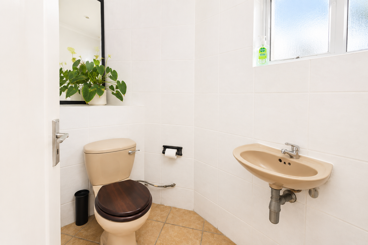 A compact guest bathroom featuring tiled walls, a wall-mounted basin, and a toilet with a wooden seat.