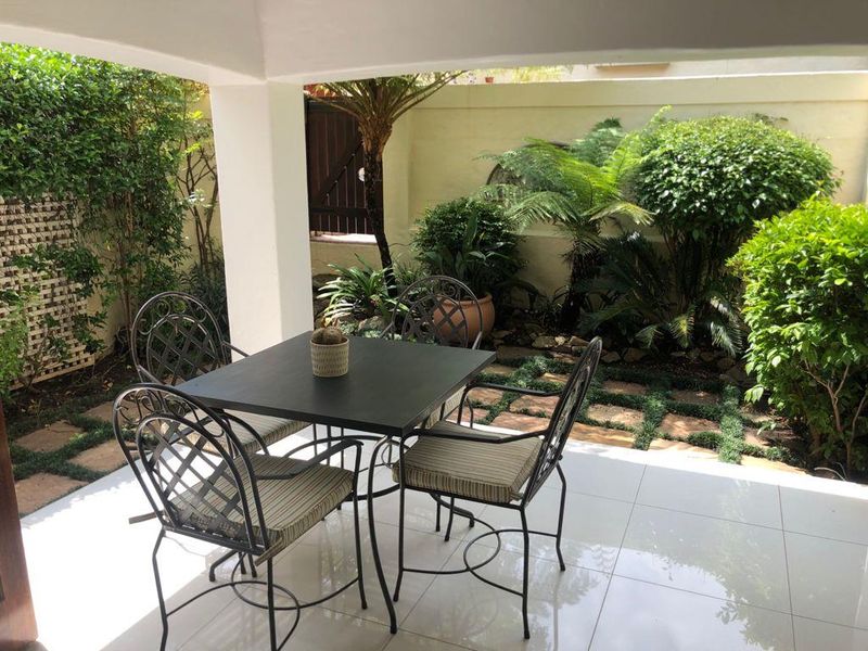 A well-maintained covered patio featuring tiled flooring, overlooking a lush, landscaped garden with a private boundary wall.
