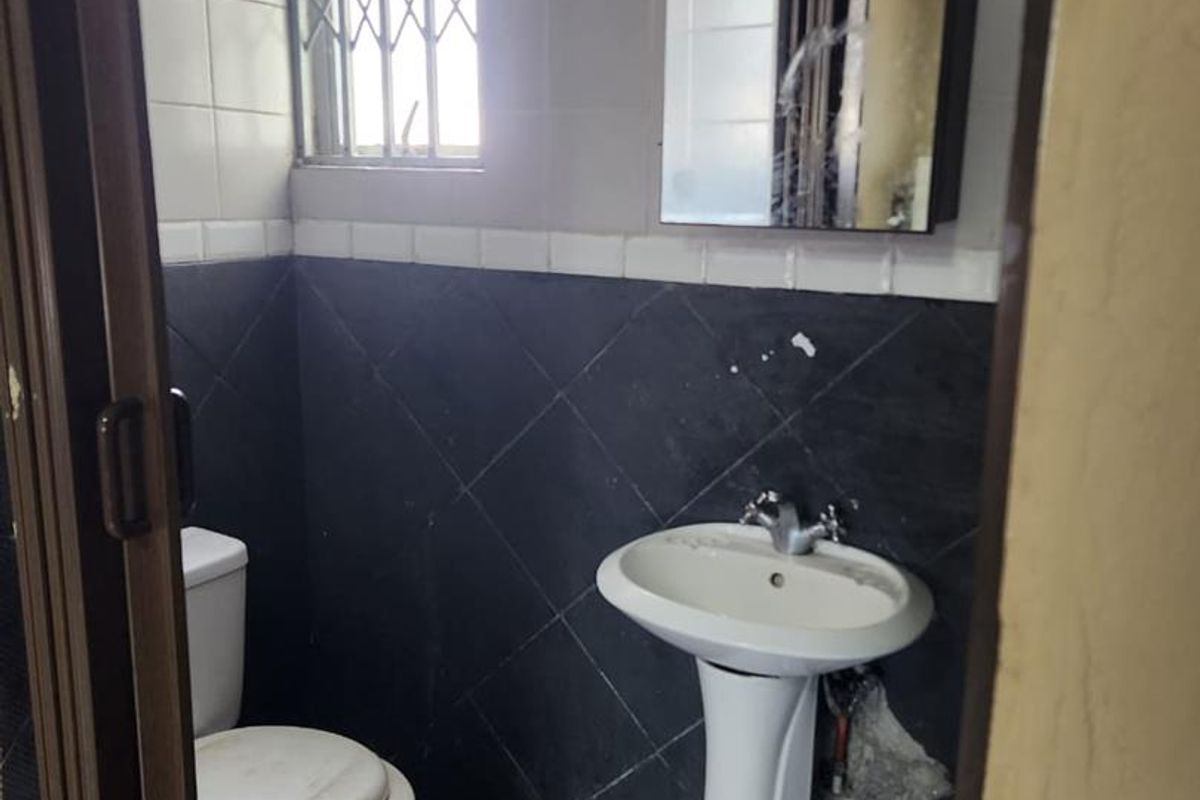 A compact bathroom featuring a pedestal basin, toilet, and tiled walls. The space requires cosmetic updates and repairs to the wall finishes.