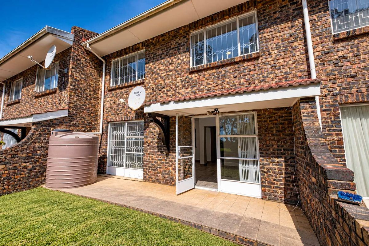 Rear exterior view of a face brick townhouse featuring a paved patio, security gates, and a water storage tank.