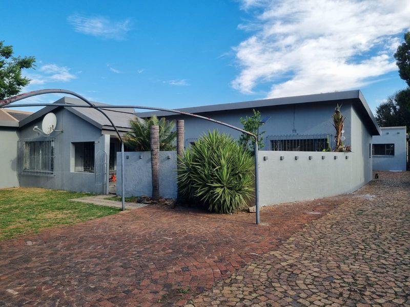 Front exterior view of the house featuring a cobblestone driveway, security bars on windows, and a low boundary wall with an arched metal entrance feature.