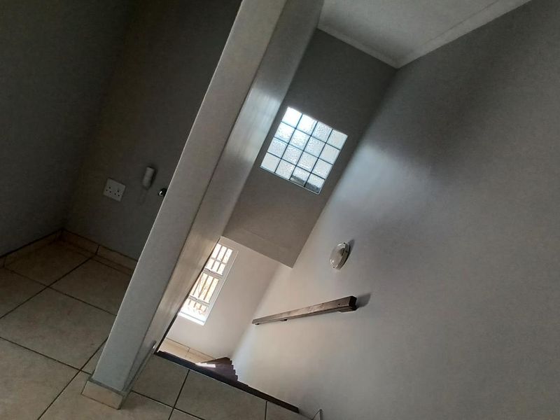 A view of an interior hallway featuring tiled flooring, a staircase with a handrail, and a glass block window providing natural light.