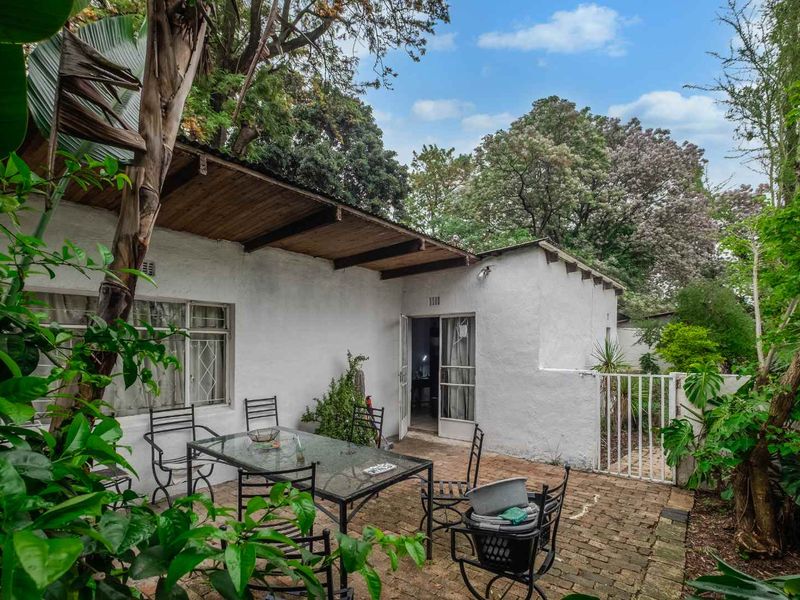 A private outdoor patio area featuring brick paving and a timber pergola, providing a quiet space for relaxation amidst the surrounding garden greenery.