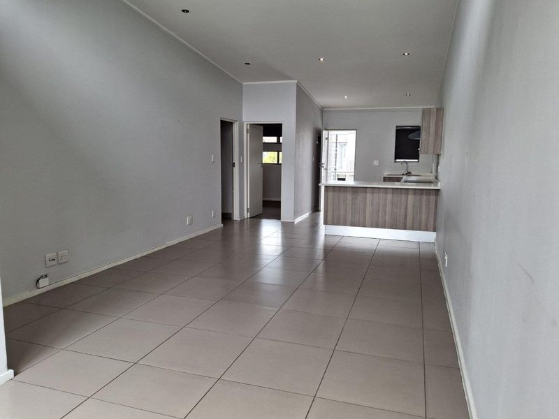 An open-plan living and kitchen area featuring neutral tiled flooring, recessed lighting, and a functional kitchen layout with a breakfast bar.