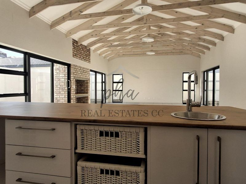Spacious open-plan living area featuring exposed timber roof trusses, a brick fireplace, and a modern kitchen island with a sink.