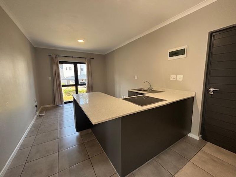 Modern open-plan kitchen and living area featuring sleek cabinetry, stone countertops, an integrated electric hob, and neutral tiled flooring throughout.
