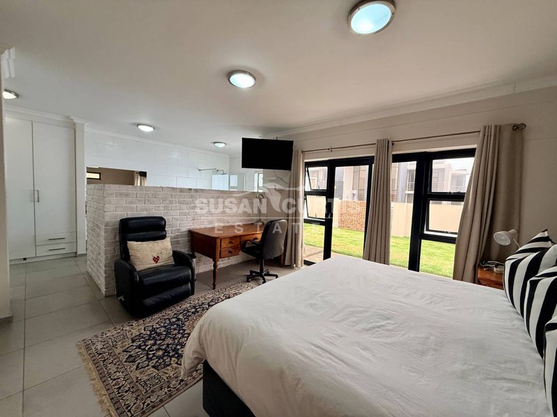 Spacious bedroom featuring a brick partition wall, built-in wardrobes, tiled flooring, and large windows providing natural light and garden access.