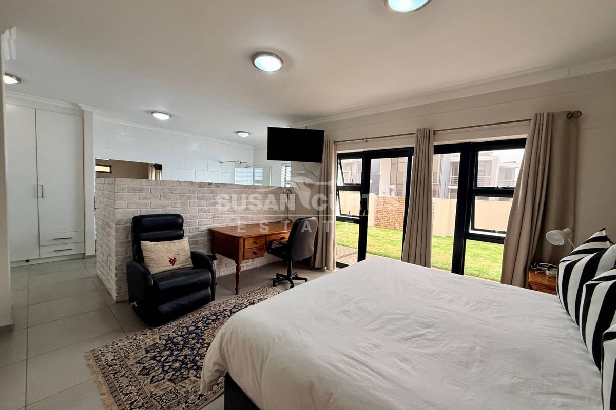 Spacious bedroom featuring a brick partition wall, built-in wardrobes, tiled flooring, and large windows providing natural light and garden access.