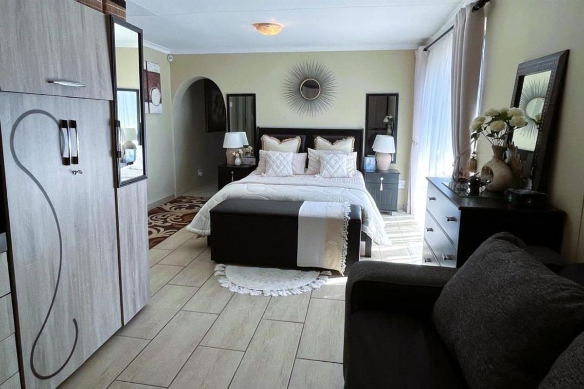 A spacious bedroom featuring tiled flooring, an arched entryway, and large windows allowing for natural light.