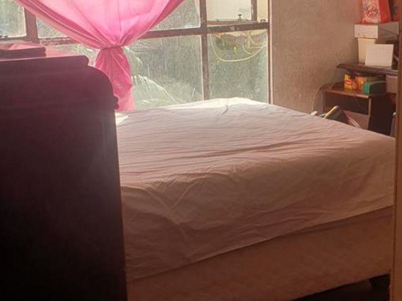 A bedroom featuring a large window with natural light, requiring cosmetic updates to the wall finishes and window frames to improve the overall condition.