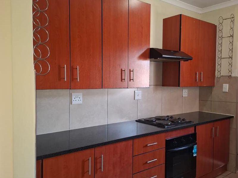 A functional kitchen featuring warm-toned laminate cabinetry, dark granite countertops, a built-in oven with gas hob, and a tiled splashback.