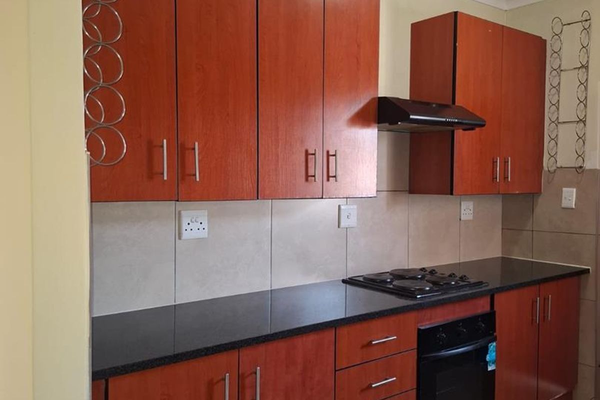 A functional kitchen featuring warm-toned laminate cabinetry, dark granite countertops, a built-in oven with gas hob, and a tiled splashback.
