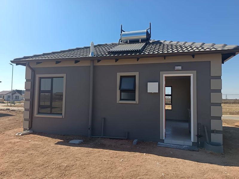Rear view of a modern house featuring a solar water heating system, tiled roof, and aluminium window frames with an open doorway.