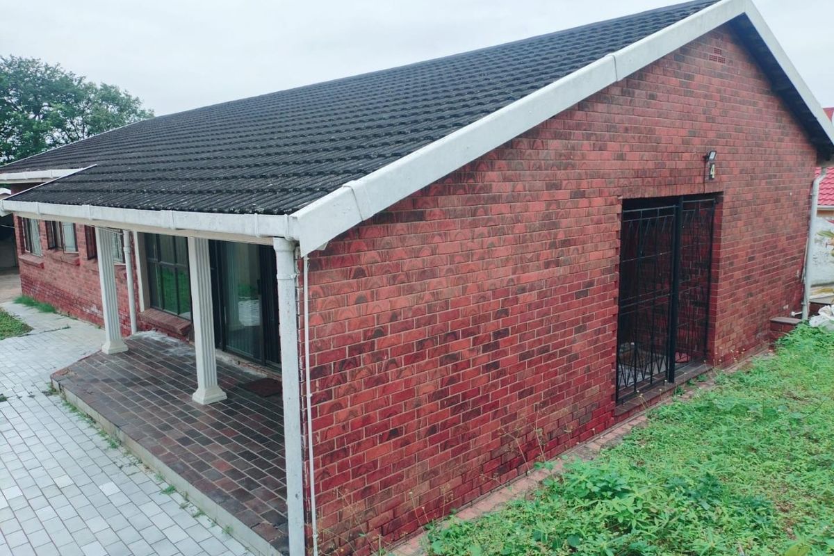 A view of the rear exterior featuring a red brick facade, a covered patio area with columns, and a tiled roof.