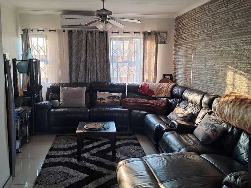 A comfortable living room featuring a textured feature wall, tiled flooring, a ceiling fan, and a wall-mounted split-system air conditioner.