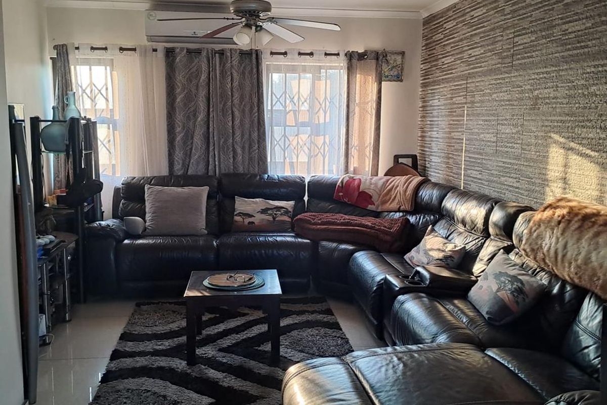 A comfortable living room featuring a textured feature wall, tiled flooring, a ceiling fan, and a wall-mounted split-system air conditioner.