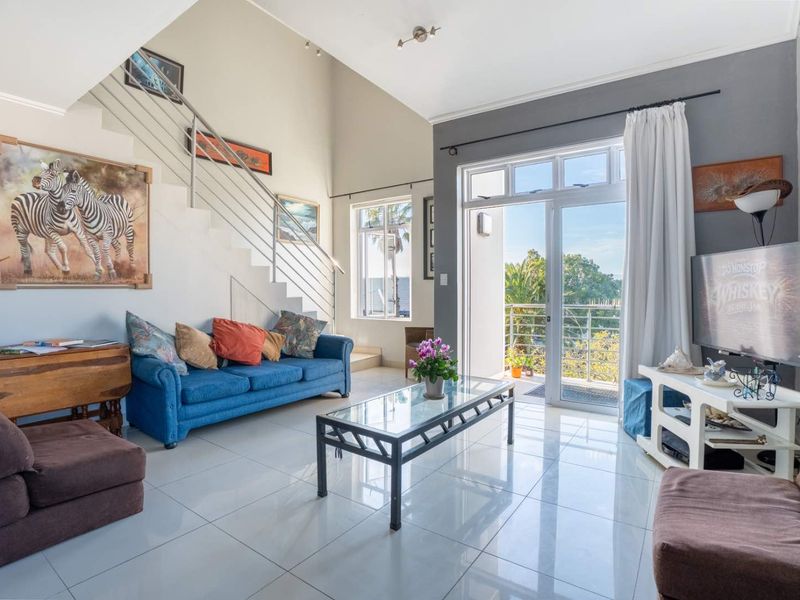 Spacious living room featuring high vaulted ceilings, tiled flooring, and a staircase with a modern stainless steel balustrade, leading to a balcony.