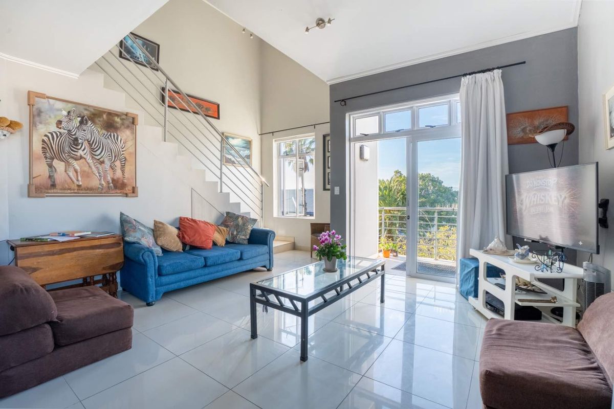 Spacious living room featuring high vaulted ceilings, tiled flooring, and a staircase with a modern stainless steel balustrade, leading to a balcony.