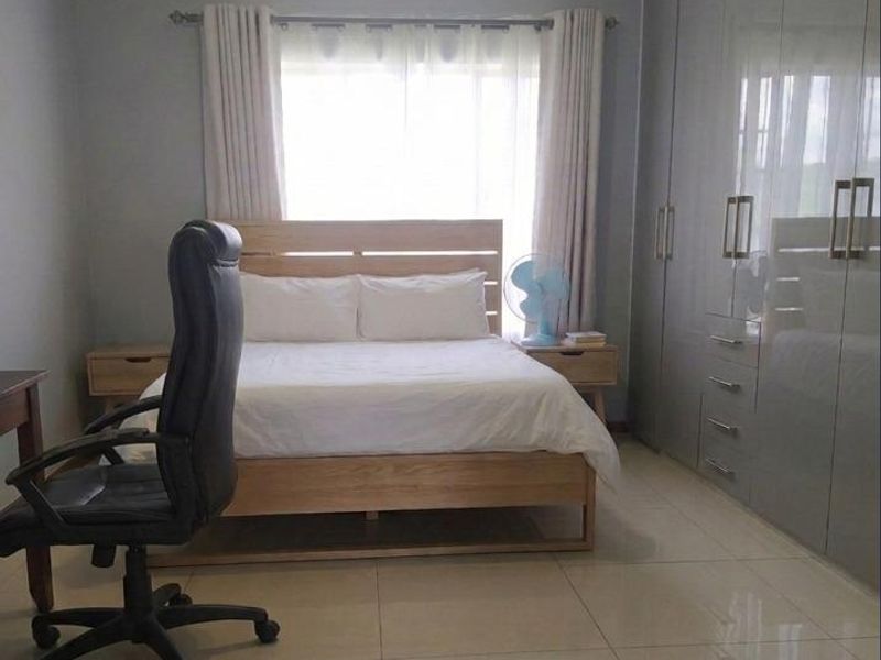 A well-maintained bedroom featuring large built-in cupboards, neutral tiled flooring, and ample natural light through the window.