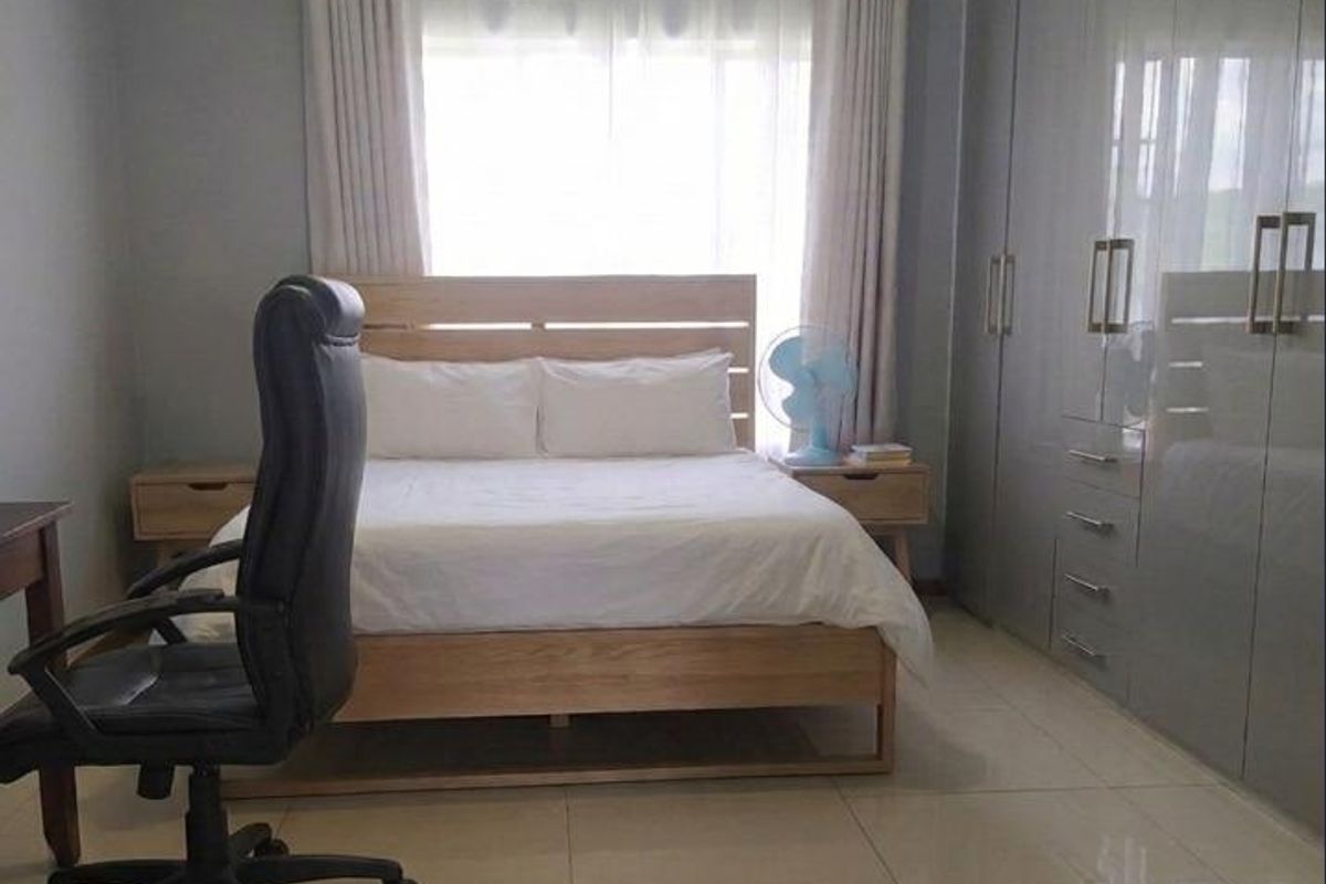 A well-maintained bedroom featuring large built-in cupboards, neutral tiled flooring, and ample natural light through the window.