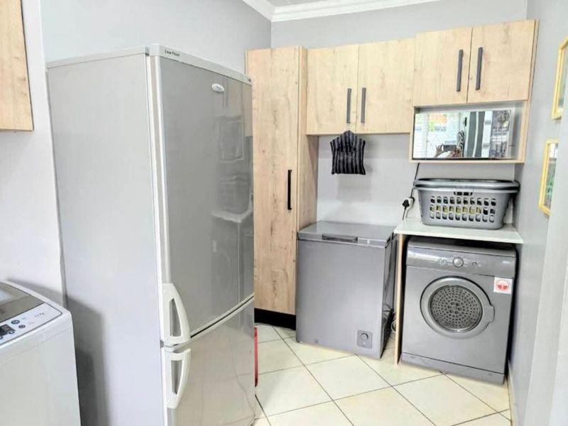 A functional laundry area featuring light wood-toned built-in cabinetry, tiled flooring, and dedicated spaces for laundry appliances.
