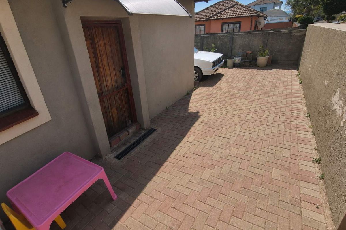 A paved rear courtyard area featuring a side entrance door with a protective awning and perimeter boundary walls.