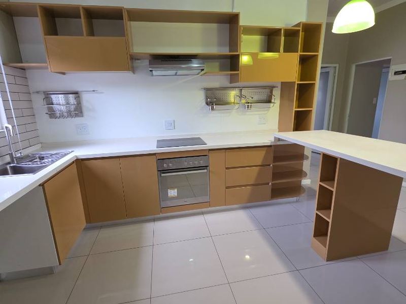 Modern kitchen featuring light wood-tone cabinetry, white countertops, integrated oven and hob, and a breakfast bar with tiled flooring throughout.
