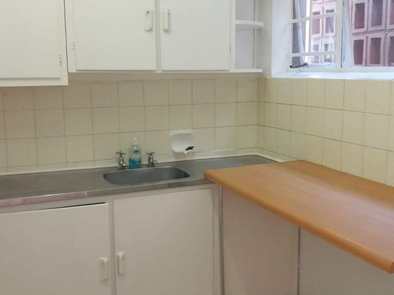 A functional kitchen area featuring laminate countertops, a stainless steel sink, and wall-mounted cabinetry with a tiled backsplash.