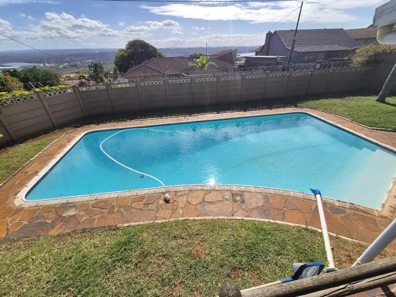 Outdoor pool area featuring a rectangular swimming pool, stone paved surround, and perimeter precast concrete walling with security fencing.