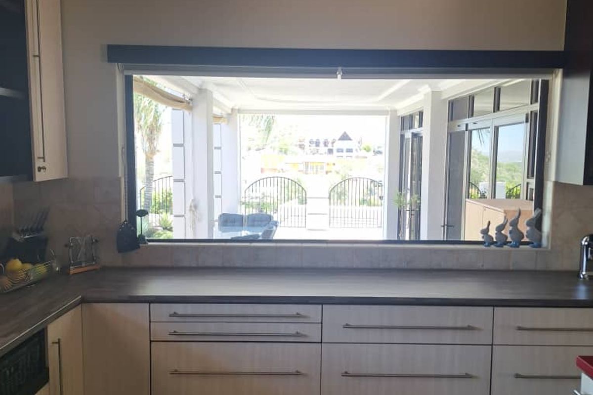 A functional kitchen featuring light-toned cabinetry, dark laminate countertops, and tiled flooring, with a large window providing a view to the outdoor patio area.