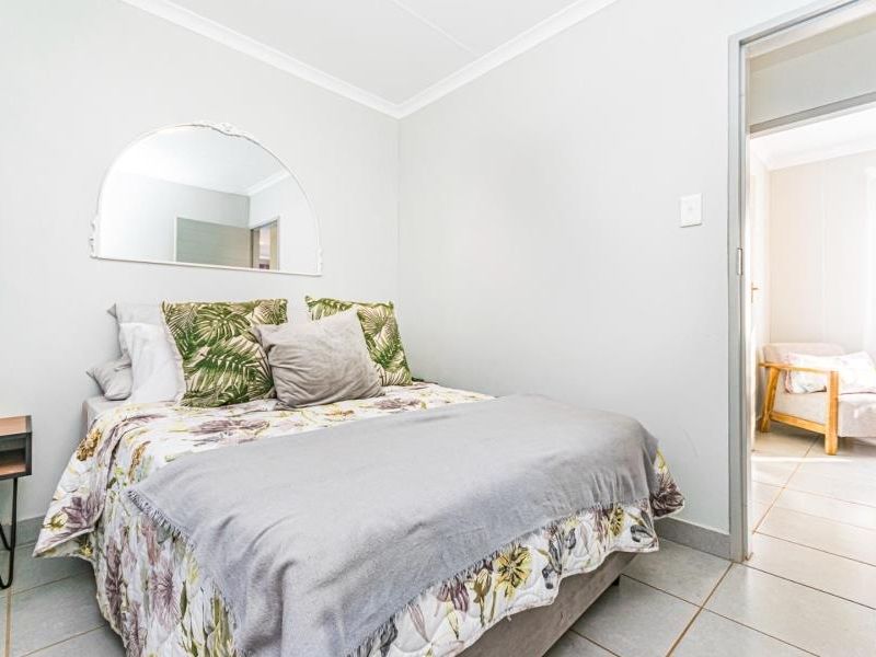 A well-maintained bedroom featuring neutral tiled flooring, cove cornicing, and a decorative wall-mounted mirror, with an adjoining room visible through the doorway.