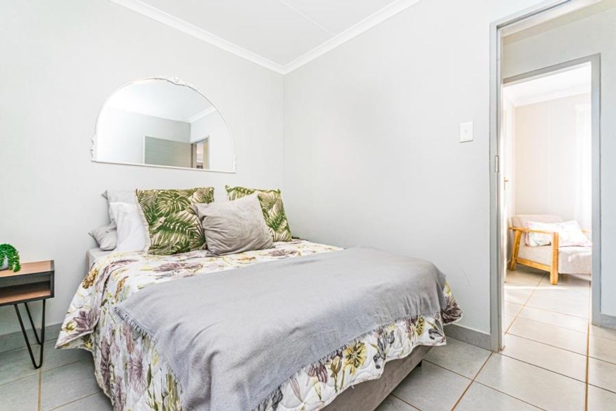 A well-maintained bedroom featuring neutral tiled flooring, cove cornicing, and a decorative wall-mounted mirror, with an adjoining room visible through the doorway.