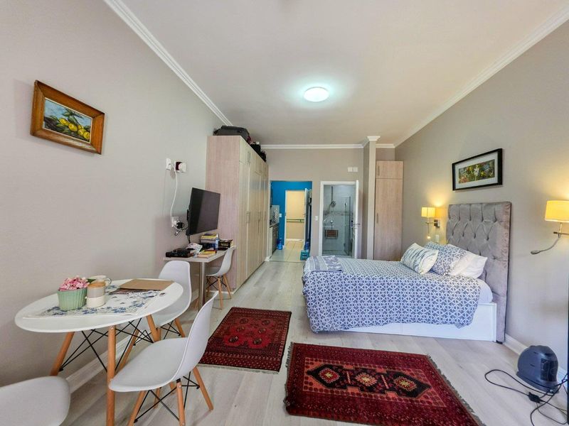 A well-maintained studio bedroom featuring light laminate flooring, built-in storage cupboards, and direct access to an en-suite bathroom.