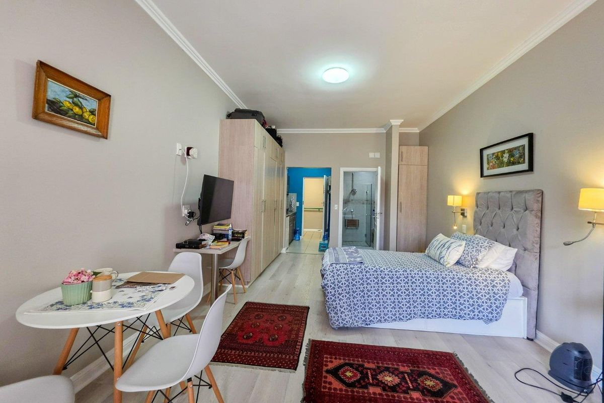 A well-maintained studio bedroom featuring light laminate flooring, built-in storage cupboards, and direct access to an en-suite bathroom.