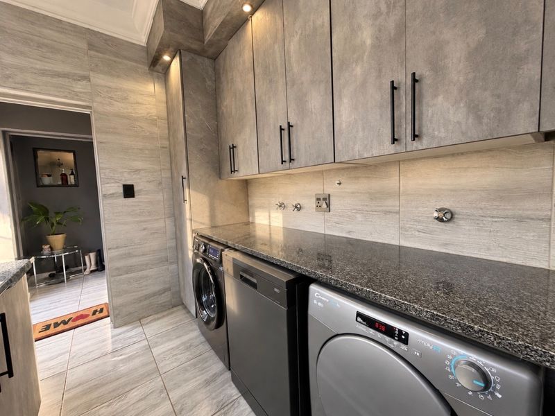 Modern laundry room featuring sleek grey cabinetry, granite countertops, tiled finishes, and integrated plumbing connections for appliances.