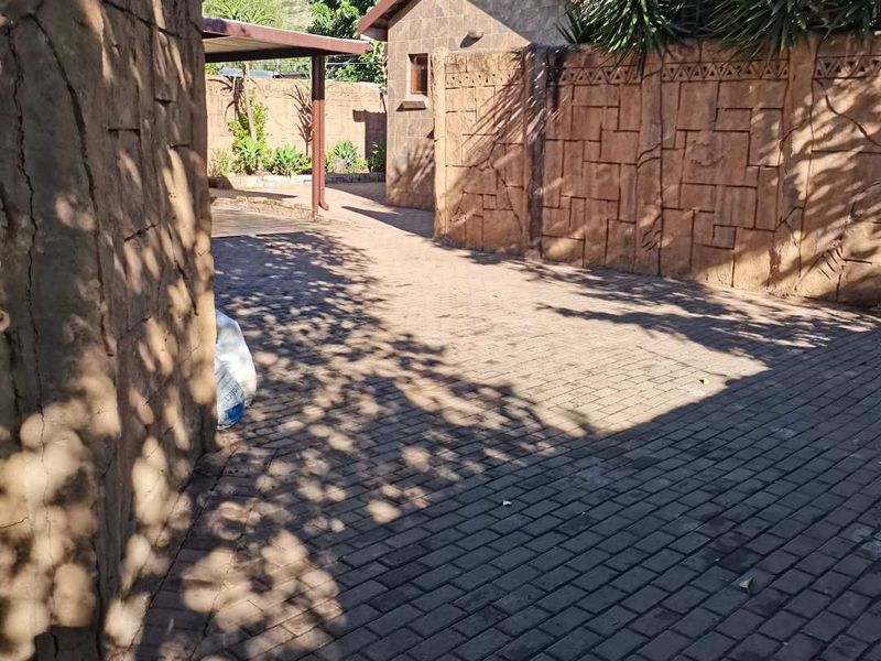 A paved rear courtyard area featuring decorative stone-clad boundary walls and a covered patio structure.