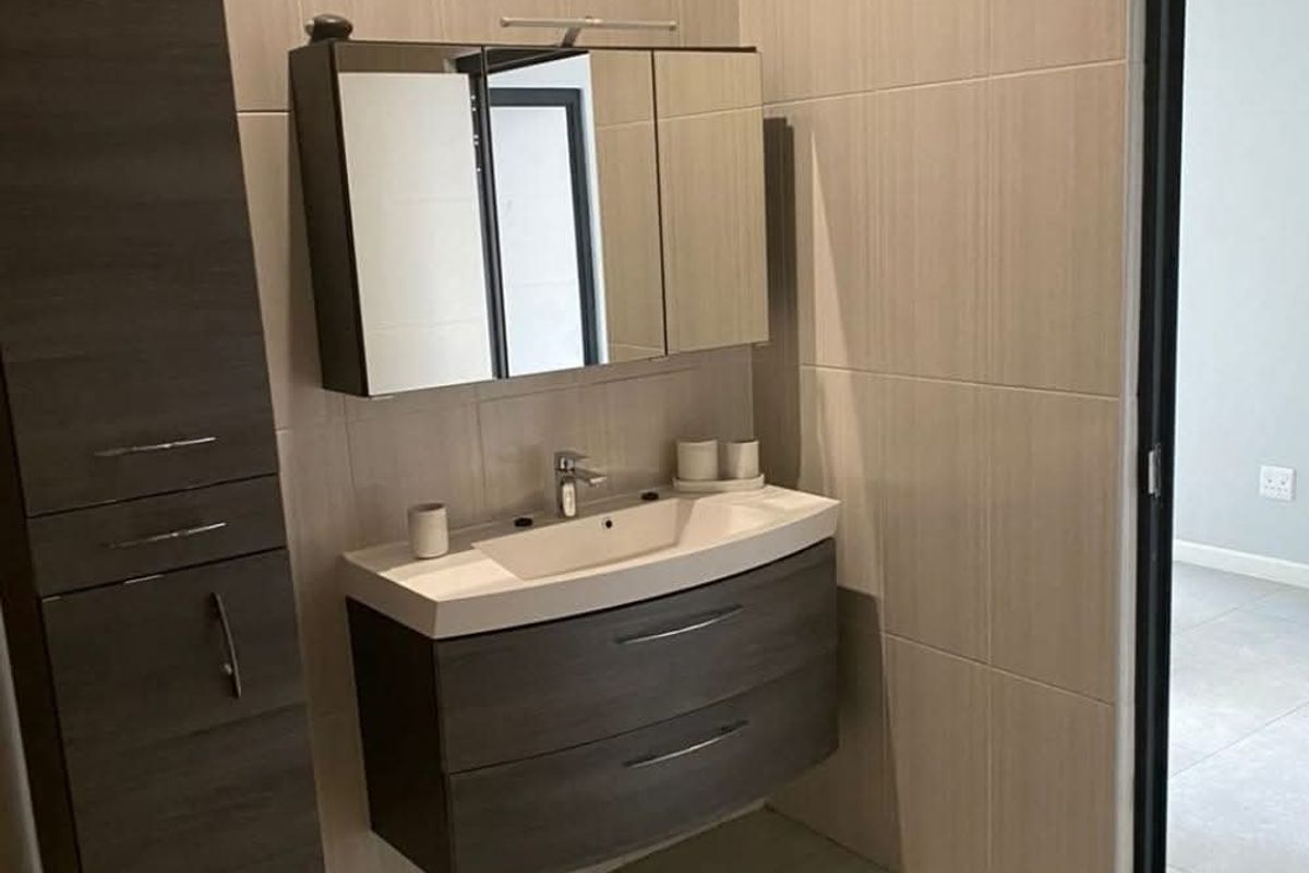Modern bathroom featuring a wall-mounted vanity with integrated basin, mirrored medicine cabinet, and tall storage unit, finished with neutral floor-to-ceiling wall tiles.