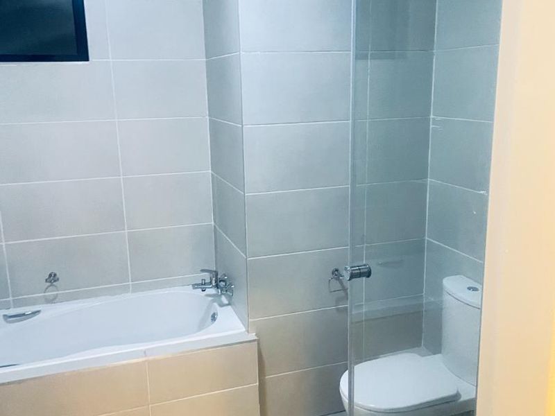 A clean, modern bathroom featuring a bathtub, a separate glass-enclosed shower, and a toilet with neutral wall and floor tiling.