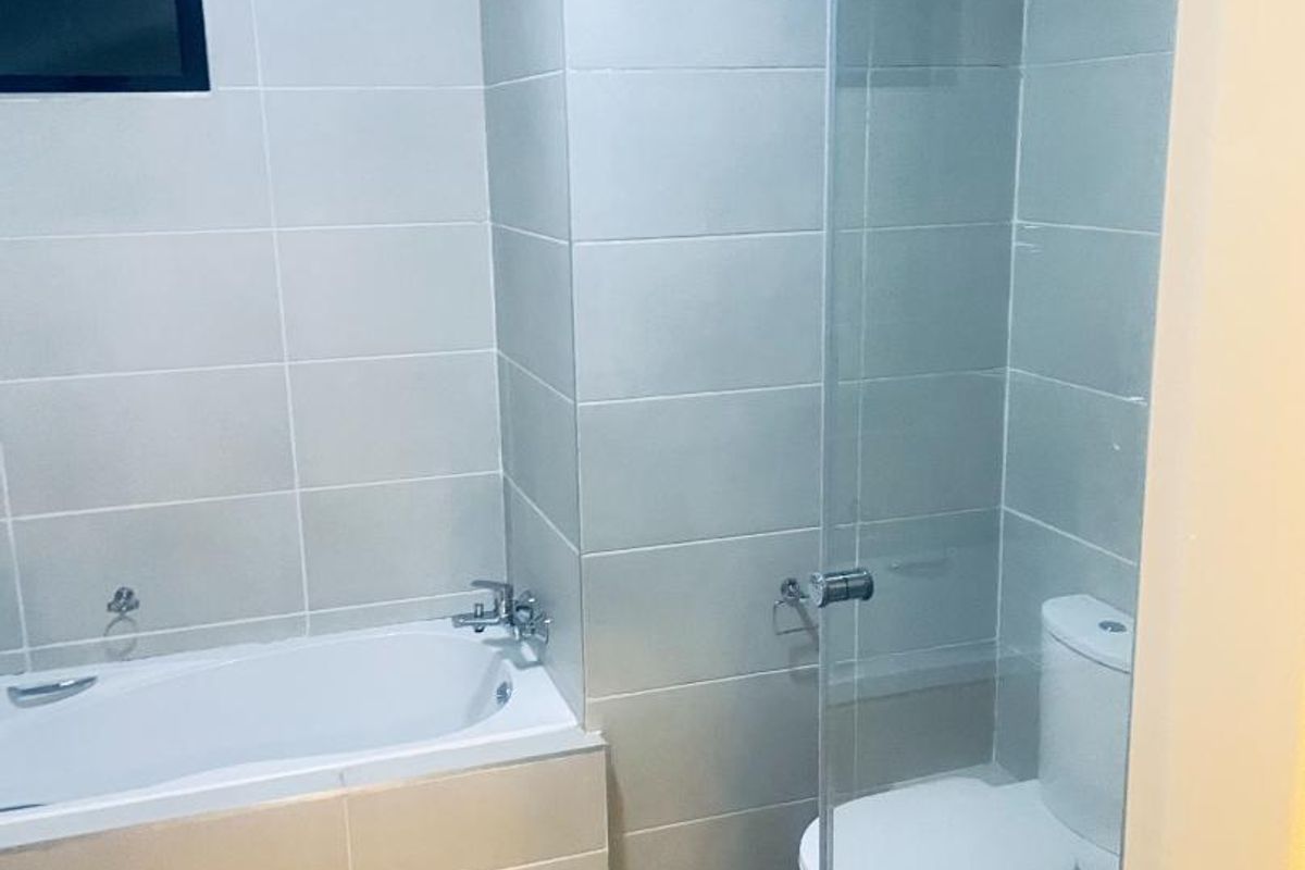 A clean, modern bathroom featuring a bathtub, a separate glass-enclosed shower, and a toilet with neutral wall and floor tiling.