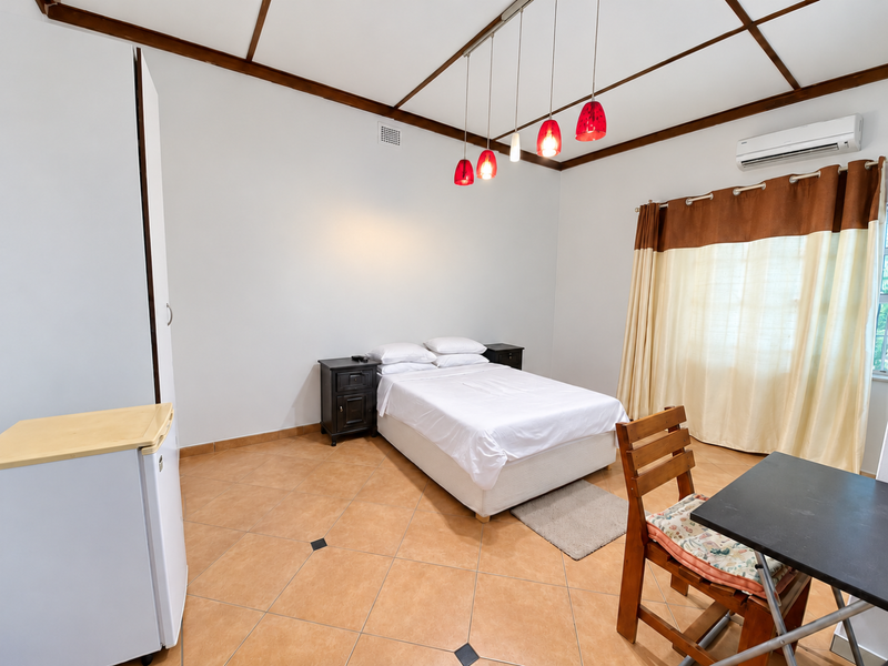 A bedroom featuring tiled flooring, exposed timber ceiling beams, a built-in wardrobe, and a wall-mounted split-system air conditioner.