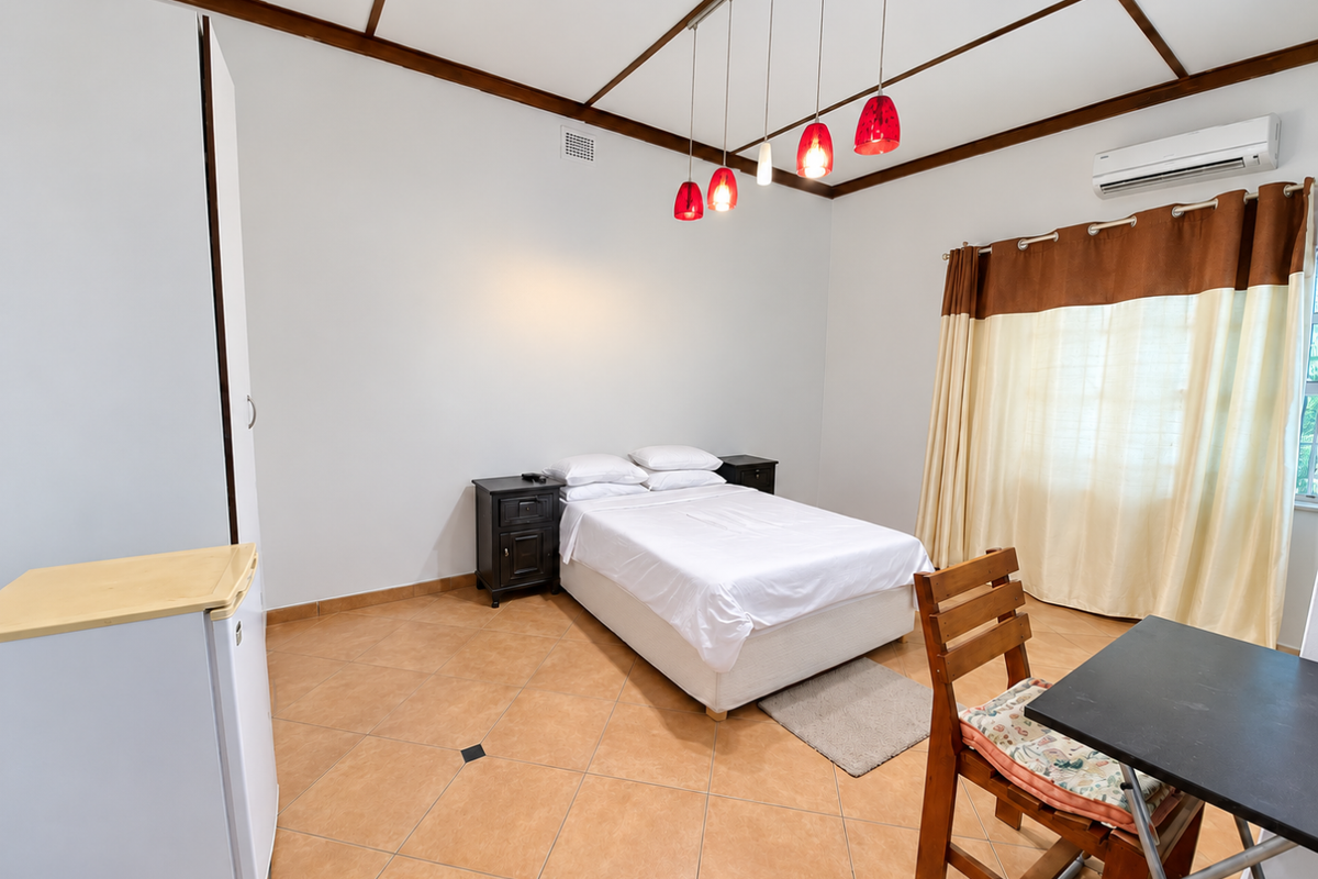 A bedroom featuring tiled flooring, exposed timber ceiling beams, a built-in wardrobe, and a wall-mounted split-system air conditioner.