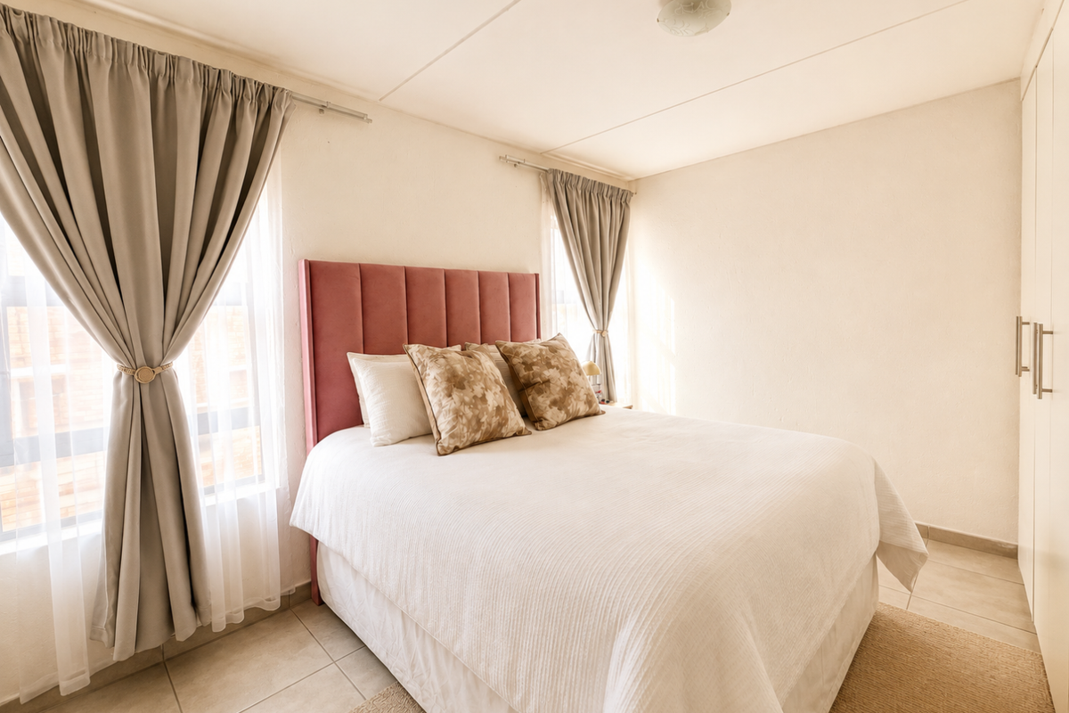 A bright and well-maintained bedroom featuring tiled flooring, built-in wardrobes, and large windows with neutral curtains.