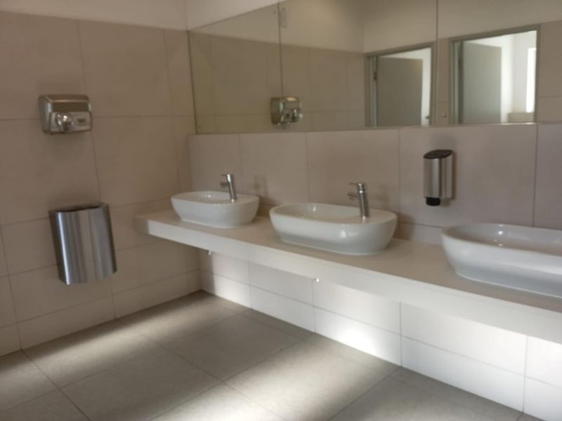 A clean, modern office bathroom featuring a floating vanity with three vessel sinks, wall-mounted faucets, and a large mirror.