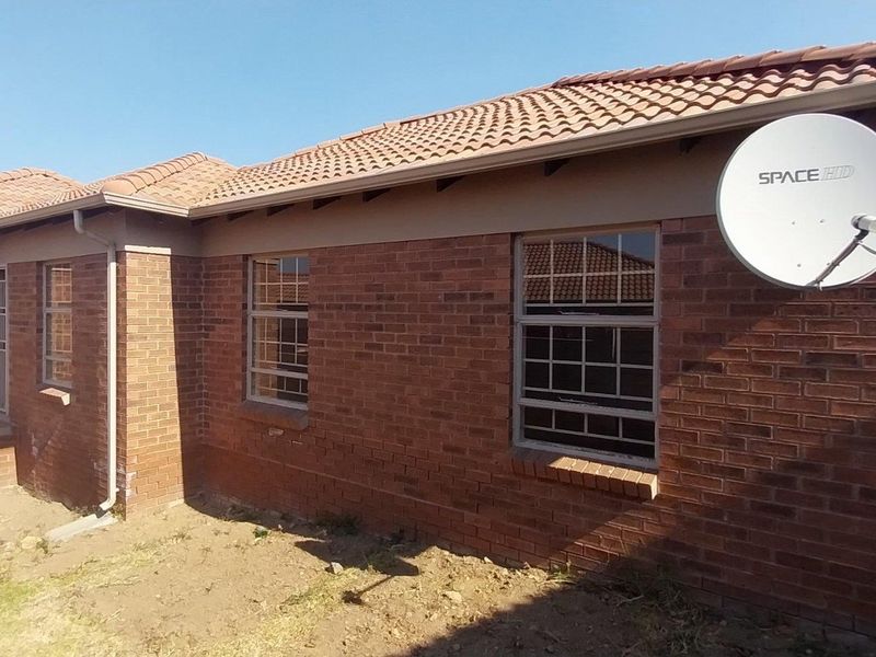 Rear view of a face brick house featuring a tiled roof, security bars on windows, and a satellite dish, with an unlandscaped yard area.