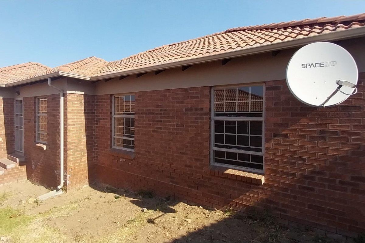 Rear view of a face brick house featuring a tiled roof, security bars on windows, and a satellite dish, with an unlandscaped yard area.
