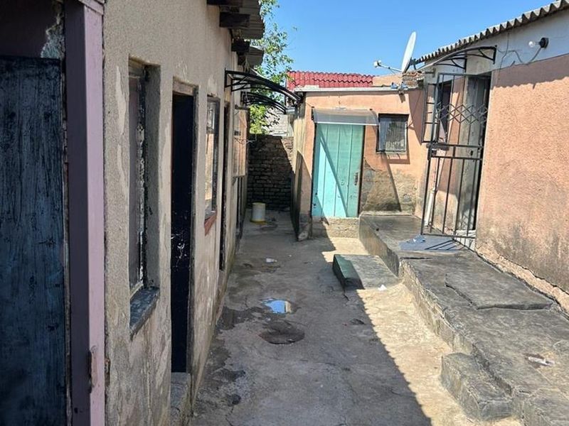 A narrow exterior rear courtyard area featuring concrete paving, multiple access doors, and weathered exterior wall finishes.