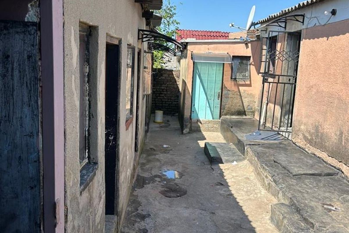 A narrow exterior rear courtyard area featuring concrete paving, multiple access doors, and weathered exterior wall finishes.
