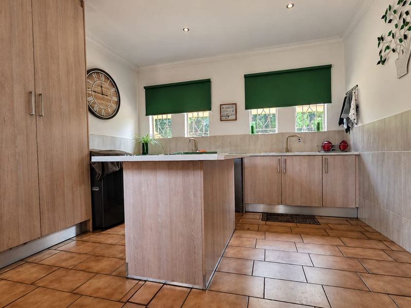A functional kitchen featuring light wood-finish cabinetry, a central island, tiled flooring, and a tiled backsplash with ample natural light.