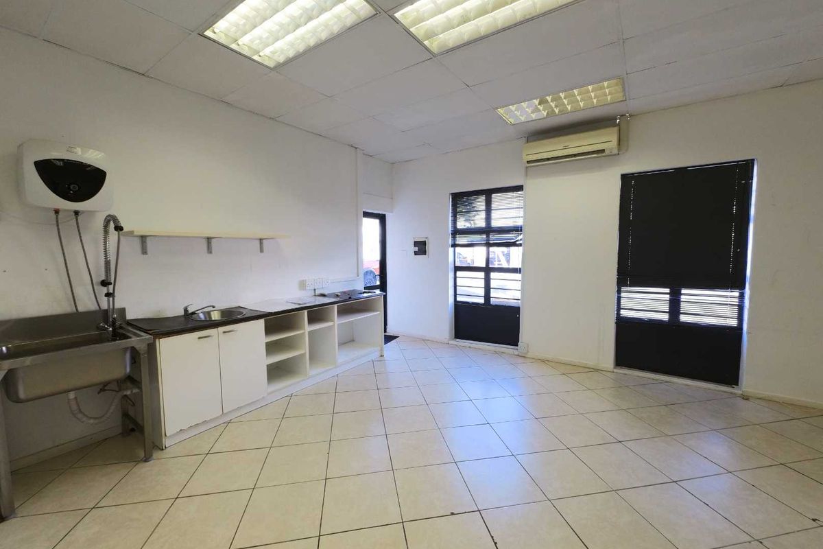 A functional industrial kitchenette area featuring a stainless steel sink, built-in cabinetry, tiled flooring, and a wall-mounted air conditioning unit.