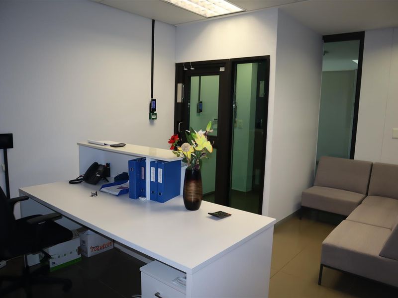 A professional office reception area featuring a built-in desk, tiled flooring, and modern glass-paneled door access.